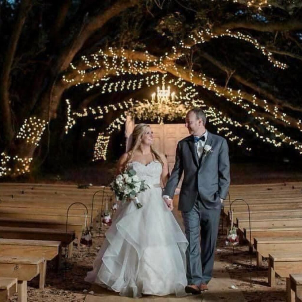 bride and groom walking under the trees at night under lights